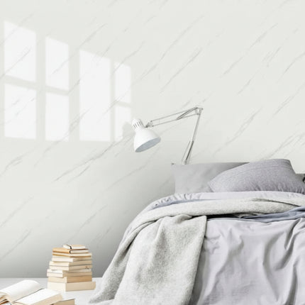 Bedroom with gray bedding, books, and a wall lamp against a white paneled wall.